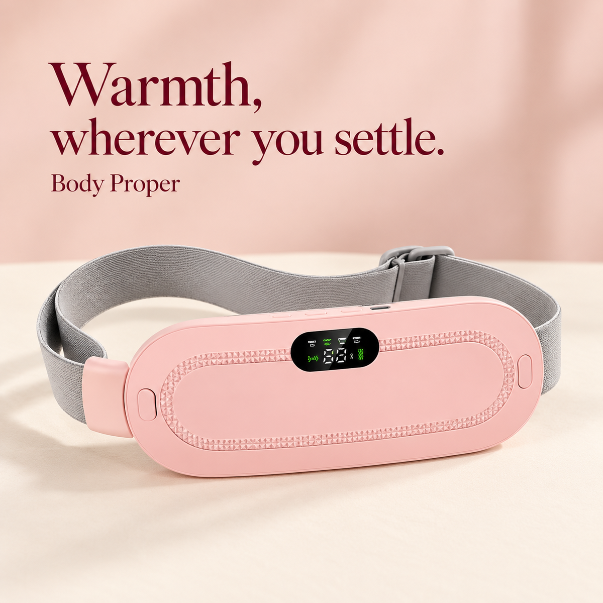 Pink wearable heating and vibration belt with grey adjustable strap on a cream background